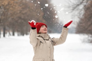 Güzel bir genç kadın bir kış günü havaya kar atıyor. Kar parkında kırmızı örgü eldivenli kız.