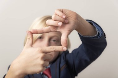 Parmaklarıyla çerçeve yapan genç bir çocuğun yakın portresi.