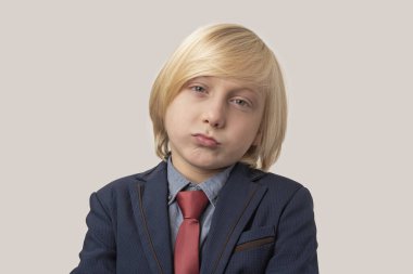 Sarı saçlı, takım elbiseli ve kravatlı üzgün bir çocuğun portresi.