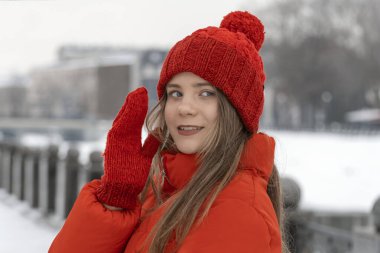 Kırmızı şapkalı ve eldivenli güzel genç bir kadın bir kış şehrinin arka planında.