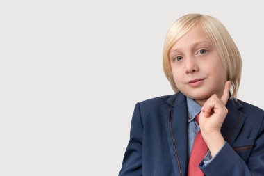 Sarı saçlı, mavi ceketli ve kırmızı kravatlı düşünceli küçük bir çocuğun portresi. Parmağını çenesinde tutuyor. Gri arka planda izole edilmiş bir şeyi düşünüyor. Halk, eğitim ve okul kavramı.