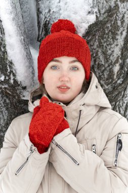 Kışın ağaçların arkasında kırmızı şapkalı ve ceketli bir kızın portresi..