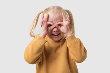 Sarı kazaklı, sarı saçlı küçük bir kızın portresi. Avuçlarına dürbün gibi bakıyor.