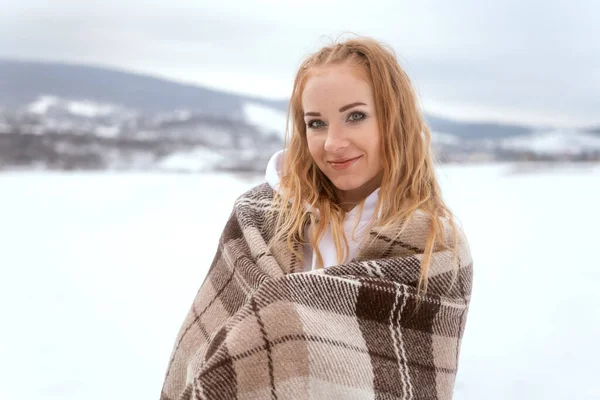 Bir kış manzarasının arka planında ekoseye sarılmış güzel genç bir kadın..