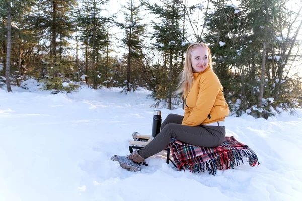Young woman had picnic in the winter park. Girl sits on sleigh with thermos. Winter holidays