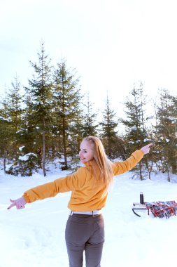 Arka planda, köknar ağaçlarının arkasındaki kış ormanında genç bir kadının portresi var. Karlı ormanda yürü. Dikey çerçeve