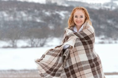 Karlı bir günde gülümseyen kızıl saçlı güzel bir kadının açık havada çekilmiş fotoğrafı. Kış zamanı