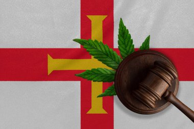 Arka planda Guernsey bayrağı ve kenevir yapraklı ahşap tokmak. Esrar bitkisinin ve uyuşturucuların yayılmasının yasadışı büyümesi