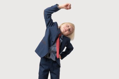 Mavi takım elbiseli ve kırmızı kravatlı şirin bir çocuk beyaz arka planda egzersiz yapıyor..