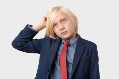 Ciddi, sarı saçlı ve kırmızı kravatlı bir çocuğun portresi, elini başının üstünde tutuyor, ciddi bir ifadeye sahip, resmi takım elbise giymiş, beyaz arka planda soyutlanmış. İnsanlar ve duygular.