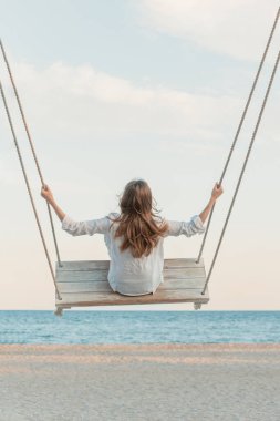 Gün batımında deniz dibinde salıncakta oturan kız. Yaz gününde sallanan genç bir kadın