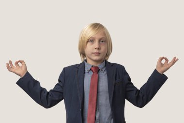Sarışın, mavi gömlekli, kırmızı kravatlı, beyaz stüdyo arka planında meditasyon yapan beyaz bir çocuk.