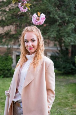 Açık havada, çiçek açan ağacın yanında bej ceketli şık, beyaz bir bayan portresi. Çekici bir genç kadın. Dikey çerçeve