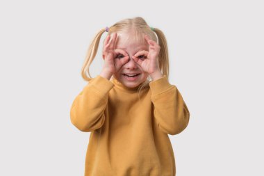 Sarı kazaklı, sarı saçlı küçük bir kızın portresi. Avuçlarına dürbün gibi bakıyor..