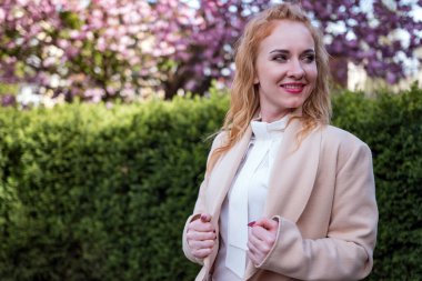 Bahar parkında gülümseyen orta yaşlı bir kadın. Beyaz bluzlu çekici genç kadın gülümsüyor. Başarılı bir iş kadını..