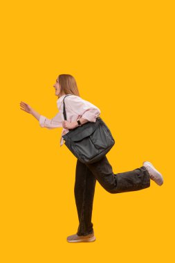 Omuz çantalı genç bir kadın geç kalıyor ve sarı arka planda birine el sallıyor..