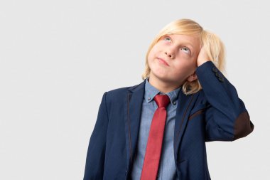 Sarı saçlı, mavi ceketli, kırmızı kravatlı, kafasını kaşıyarak düşünen beyaz bir gencin portresi. Beyaz arkaplanda izole