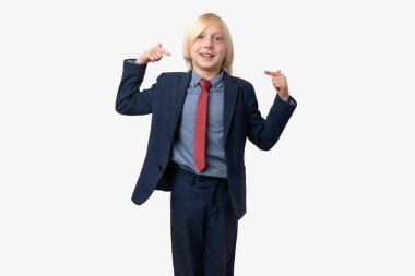 Mavi takım elbiseli ve kırmızı kravatlı küçük sarışın bir çocuğun portresi kendini işaret ediyor ve gülümsüyor.