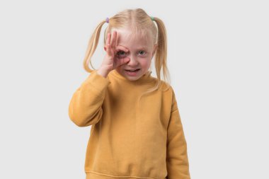 Sarı kazaklı küçük bir kızın portresi tamam jest gösteriyor ve beyaz arka planda izole bir şekilde kameraya bakıyor.