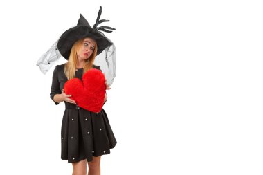 Sad witch in Halloween costume holds a red heart, looking unhappy and heartbroken in a spooky studio portrait. clipart