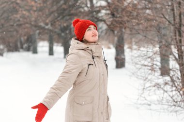 Genç bir kadın kışın parkta yürüyor. Kırmızı şapkalı ve ceketli mutlu kız.