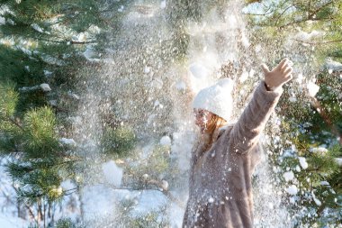 Genç bir kadın havaya kar fırlatıyor. Kış ormanında kar yağışı