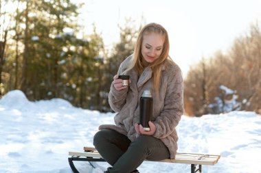 Kışın ormanda bir fincan kahveyle güzel genç bir kadın..