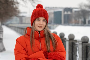 Kış şehrinin arka planında kırmızı örgü şapkalı bir kızın portresi..