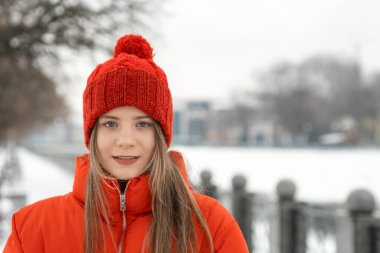 Mavi gözlü, uzun saçlı, kırmızı örgü şapkalı ve kırmızı ceketli kızın portresi..