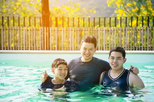父亲和他的两个儿子在清澈的水游泳池里玩耍 幸福的家庭玩时间概念 — 图库照片