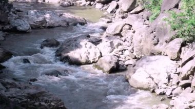 Yavaş çekim vahşi dağ nehri taştan kayaların arasından akar, ormanın derinliklerinde akan küçük akarsu güçlü güneş ışığı ve gölgesi ile, yeşil ekoloji barışçıl çevre kavramı
