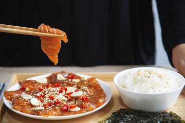 Yakın plan kadın, terbiye edilmiş somon alabalığını toprak sosunda, sarımsak ve biberi pirinç ve çarşaf yosunuyla yiyor. Meşhur Kore yemeği tarzı.