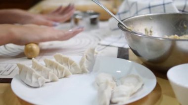 Eller gyoza hamurunu titizlikle un kaplı bir yüzeyde yuvarlıyor, arka planda merdane ve süzgeç gibi mutfak aletleriyle Japon hamur işi ambalajları yapma sürecini gözler önüne seriyor.