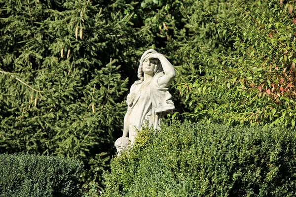Statue of the woman looking towards the sun wih hand shading in the green bush