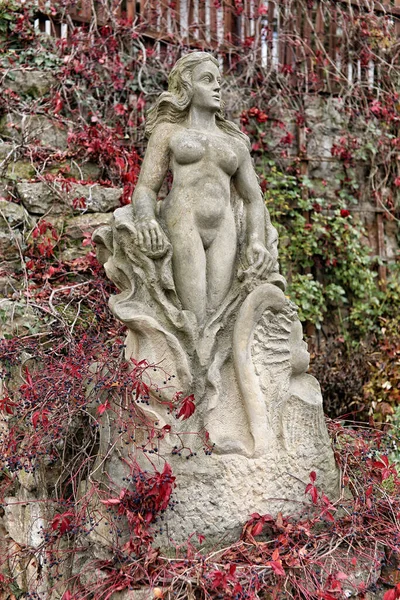 赤い花と庭の丘の上の岩の中の裸の女性の像 — ストック写真