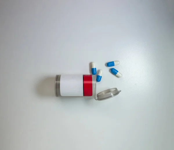 白い表面や背景に瓶の外にカプセルや錠剤がこぼれた処方薬のためのオープン透明なボトルの上のビューを閉じます — ストック写真