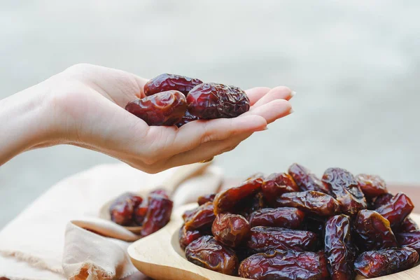 Bir hurma ağacını ahşap bir fincanda tutan el, yüksek enerji sağlayan ve yorgunluğu azaltan kahverengi kurumuş bir meyvedir. Müslümanlar oruç tutarken yer. (Ramazan ayı).