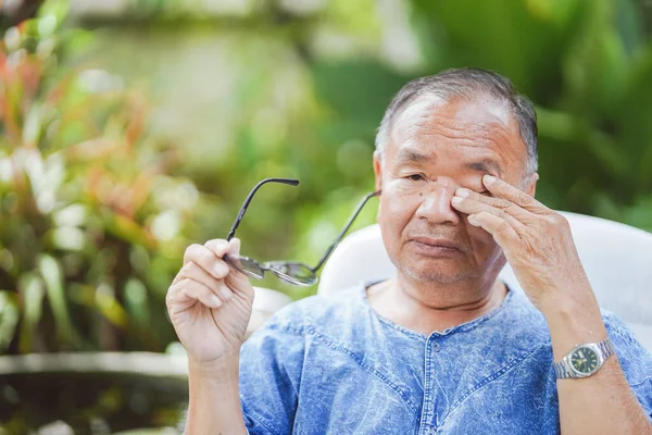 Elderly man rubbing his eyes while holding glasses due to overuse of the eyes, causing itching and irritation.