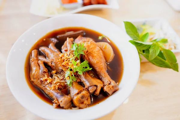 Braised chicken noodles or braised chicken leg in white bowl on table in restaurant, Thai street food, tasty food of Thailand.