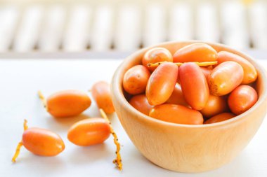 Tahta bir kasede taze tarihler beyaz bir masada bulanık doğal bir arka plan.