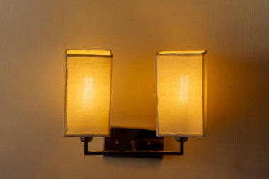 The bedside lamp on the wall shines a warm glow. Bedroom decoration.