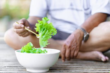Man's hand picking up lettuce with a fork from a white bowl. Healthy food concept.