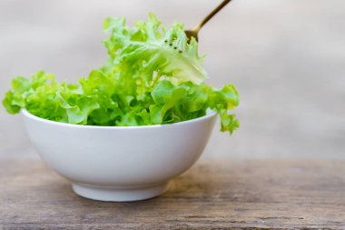A fork that picks up salad from a white bowl on a wooden background. Healthy food concept.