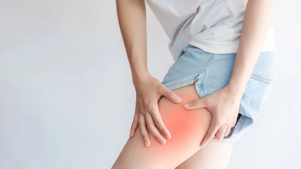 A woman touches her thigh due to pain or inflammation in the muscles.