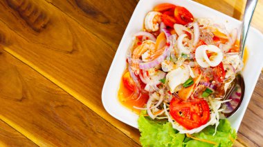 Tahta bir masaya yerleştirilmiş beyaz tabakta deniz ürünleri salatası, üst manzara, baharatlı Tayland yemeği..
