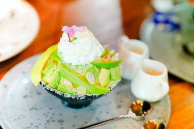 Siyah bardakta yeşil avokado bingsu lezzetli bir tat ve ahşap masada yoğunlaştırılmış süt..