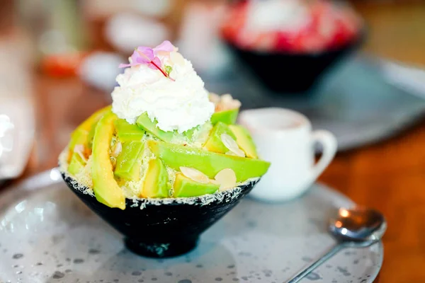 Siyah bir fincanda yeşil avokado bingsu ve kafedeki bir masada iştah açıcı bir kaşık..