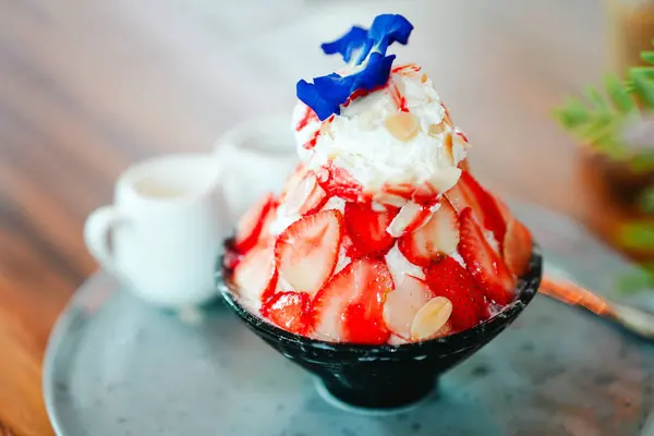 Sulu kırmızı çilekli bingsu nefis bir tatlıdır ve kafe masasındaki bir bardakta kesilmiş buzdur..