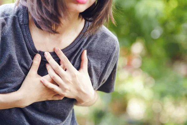 Asian woman has chest pain so she holds her hand to her chest in pain. Health care concept.