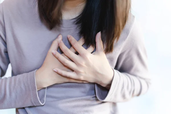 Asian woman has chest pain so she holds her hand to her chest in pain.